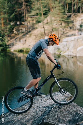 young trial biker balancing on rocky cliff over lake © LIGHTFIELD STUDIOS
