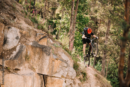 trial biker riding downhill outdoors in pine forest