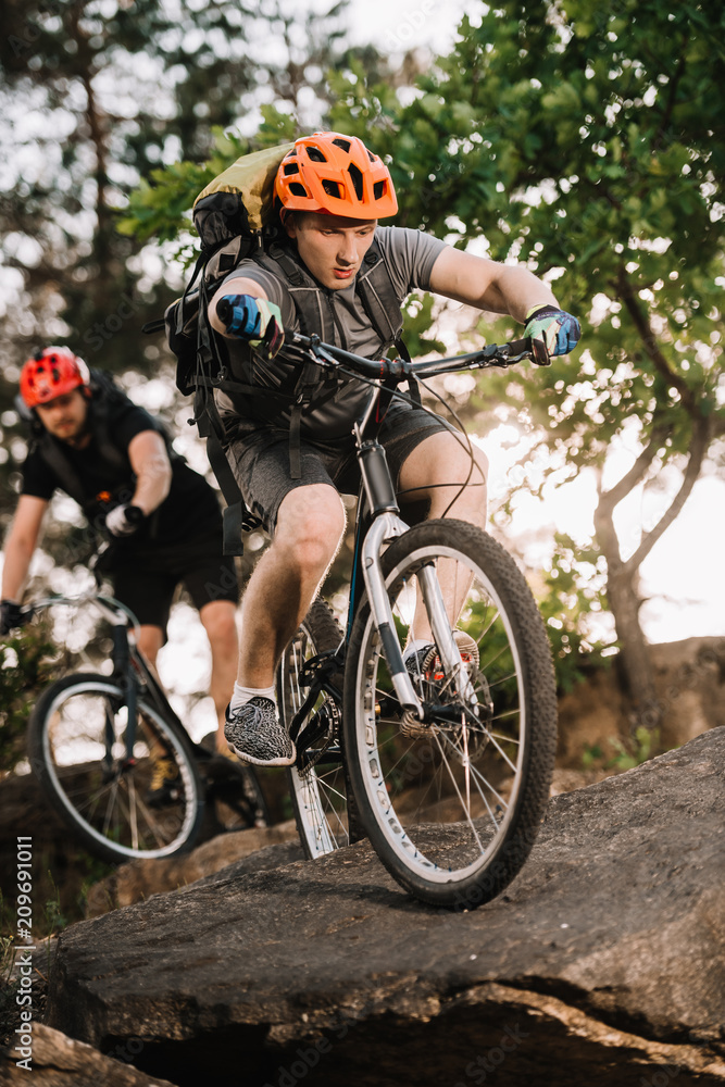 Obraz premium active young trial bikers riding on rocks at pine forest