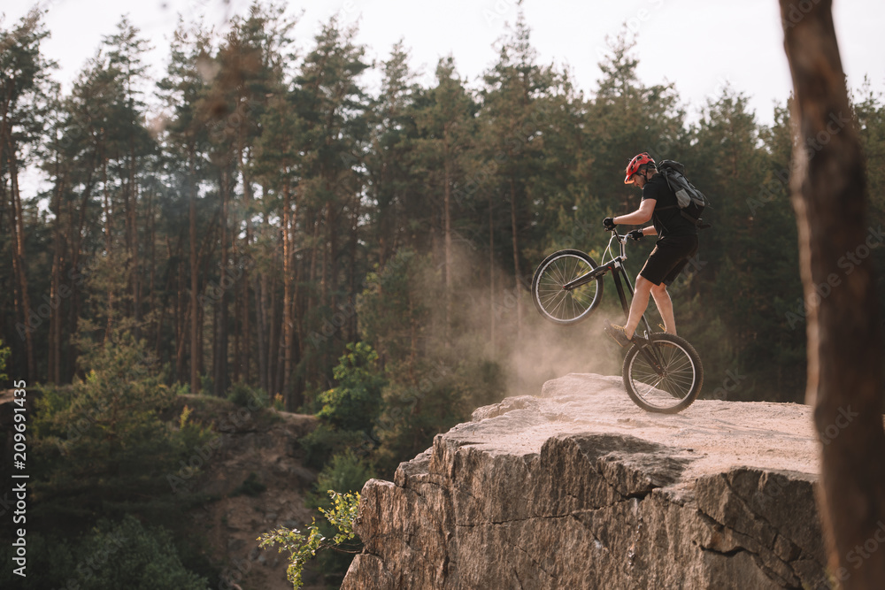 Fototapeta premium trial biker balancing on back wheel on rocks outdoors