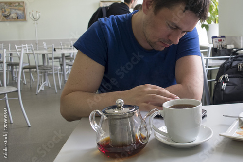 A man is sitting in a cafe on the table and a kettle, a man is looking something in the mobile phone