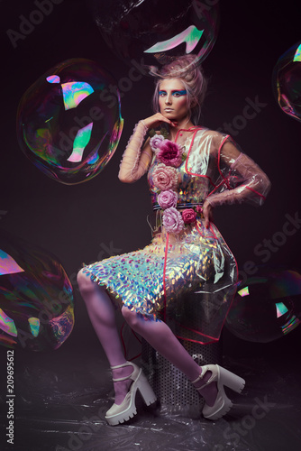 Gorgeous woman in biofuture pompadour style. Female in fashion transparent raincoat with splendid make up and hairstyle, photoshoot through soap bubble photo