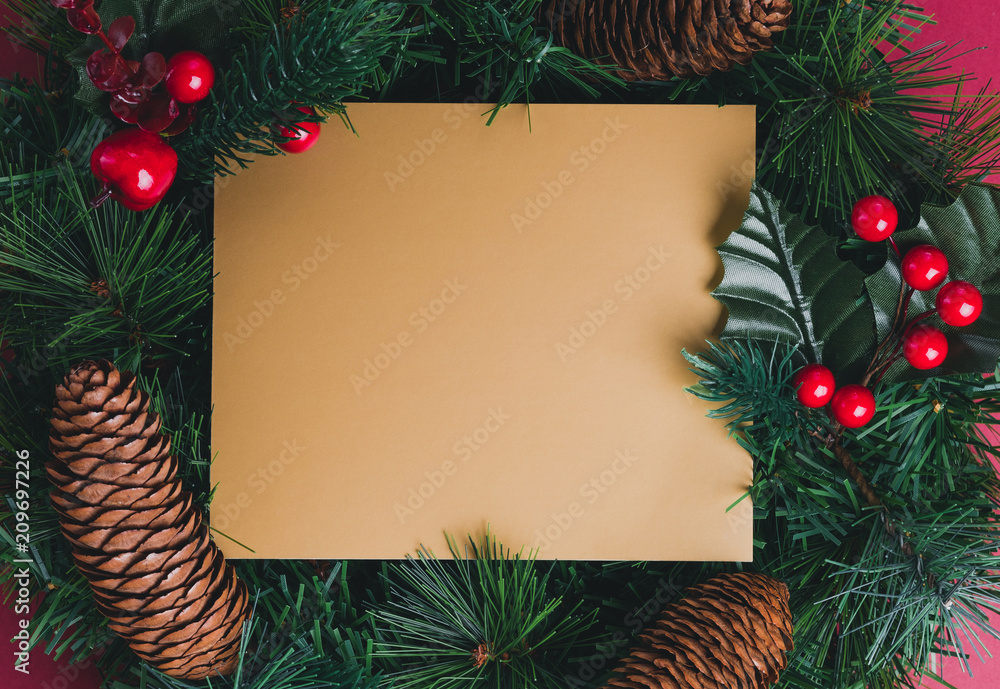 Gold blank greeting card on Green pine christmas wreath with pine cone ,cherry decoration item on red background.Mock up template for adding text or design.Celebration holiday festive concept. Gold blank greeting card on Green pine christmas wreath with pine cone ,cherry decoration item on red background.Mock up template for adding text or design.Celebration holiday festive concept.
