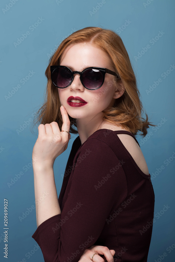 Naklejka premium beautiful girl with makeup and red lips in sunglasses on blue background