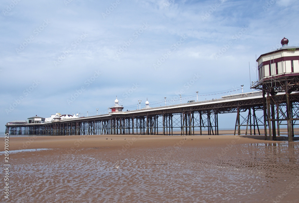 view of the historic victorian north pier in blackpool with the kiosks and buildings with the beach visible at low tide on a bright sunny summers day