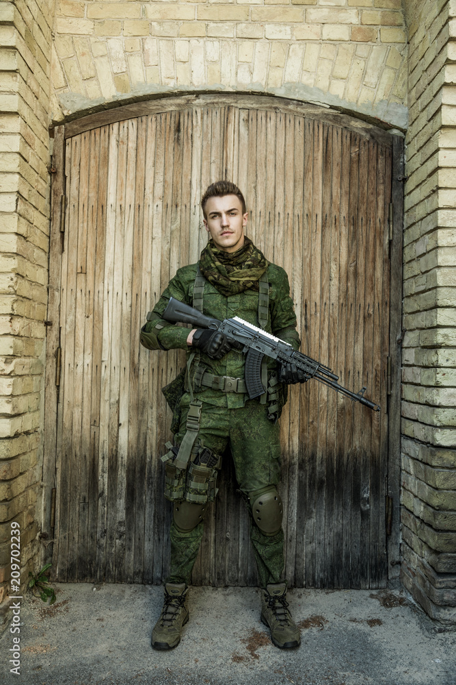 Young male military soldier with a rifle posing against wooden background