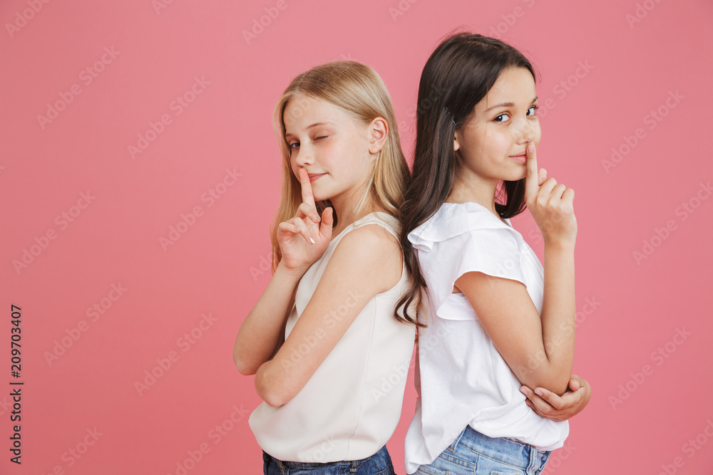 Photo of amusing little girls 8-10 years old wearing casual clothing holding index finger on lips and asking to keep silence or secret, isolated over pink background Photo of amusing little girls 8-10 years old wearing casual clothing holding index finger on lips and asking to keep silence or secret, isolated over pink background