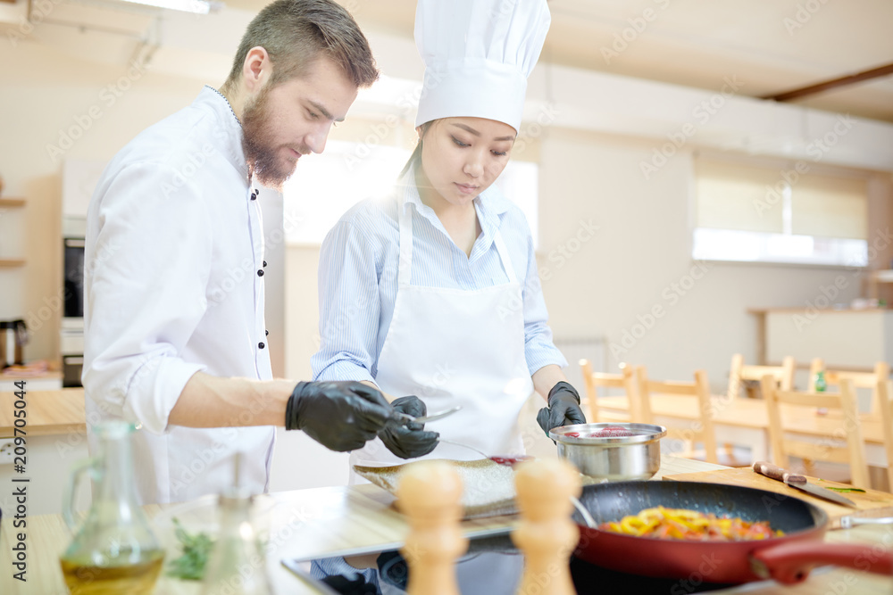 Portrait of two professional chefs cooking delicious dishes in modern kitchen, copy space Portrait of two professional chefs cooking delicious dishes in modern kitchen, copy space