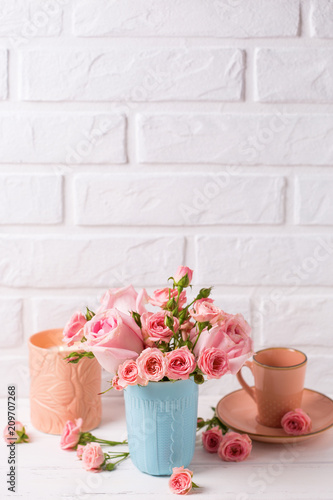 Pink roses flowers in blue cup, burning candle and little cup