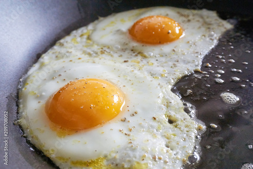 Close-up of two fried eggs with salt and pepper in a frying pan
