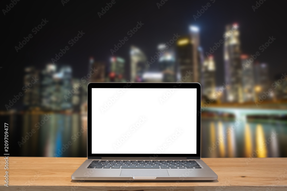 Modern computer,laptop with blank screen on wood table with office window view on blurry singapore night city background Modern computer,laptop with blank screen on wood table with office window view on blurry singapore night city background