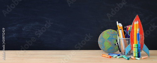Back to school concept. rocket, earth globe and pencils in front of classroom blackboard.