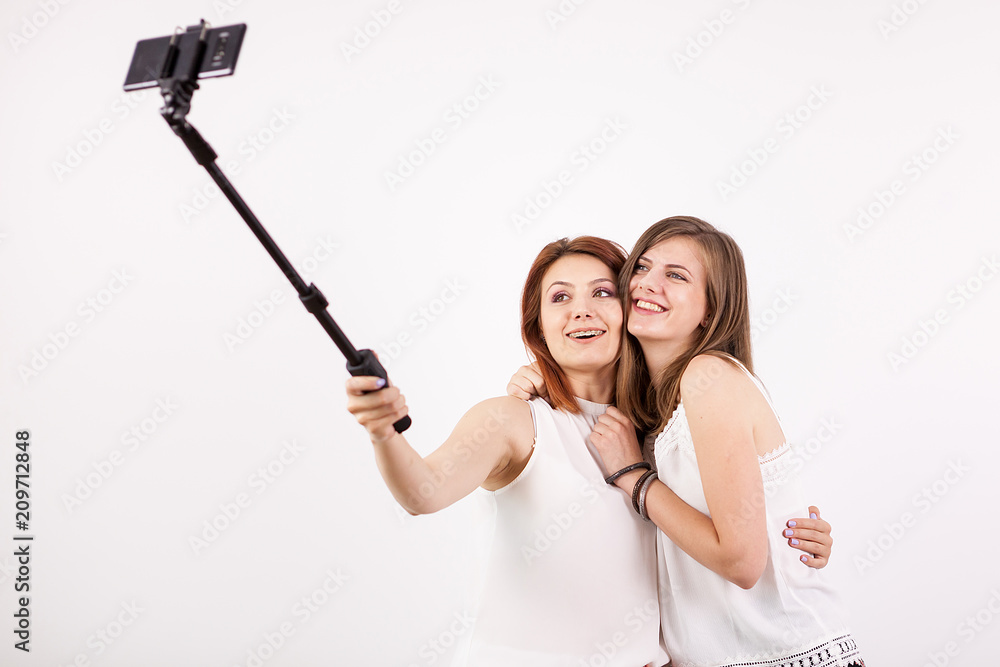 Two beautiful young woman taking a selfie with a selfie stick and making different funny and silly faces while doing it. Studio photo over a white wall Stock Photo | Adobe Stock Two beautiful young woman taking a selfie with a selfie stick and making different funny and silly faces while doing it. Studio photo over a white wall Stock Photo | Adobe Stock