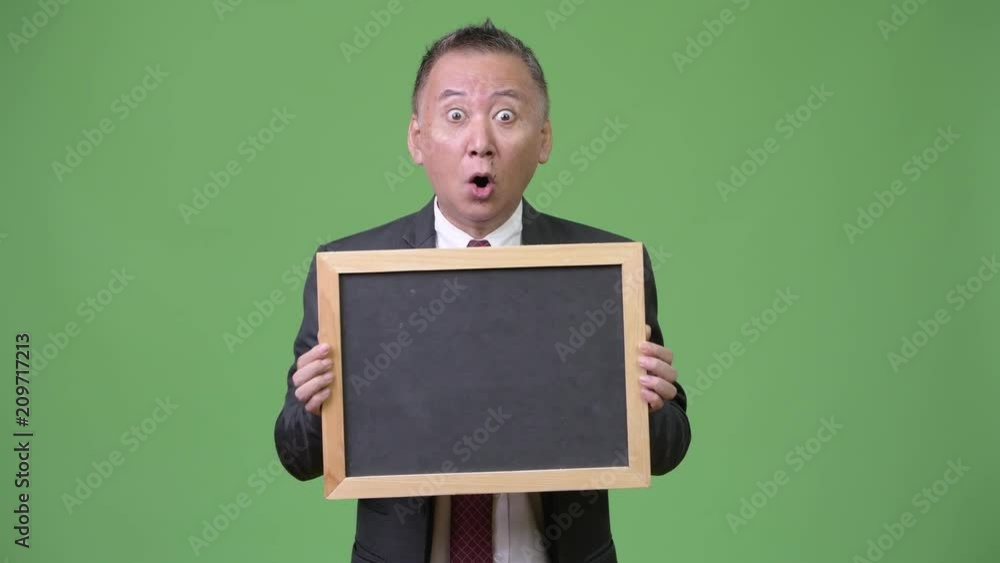 Mature Japanese businessman holding blackboard against green background Mature Japanese businessman holding blackboard against green background