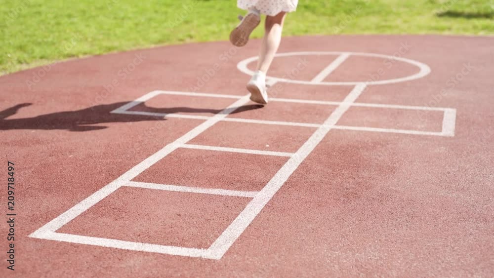 Little girl jumping while playing Hopscotch at park. Cute girls on children playground outdoors. Legs of kids jumps hopscotch on asphalt. Little girl jumping while playing Hopscotch at park. Cute girls on children playground outdoors. Legs of kids jumps hopscotch on asphalt.