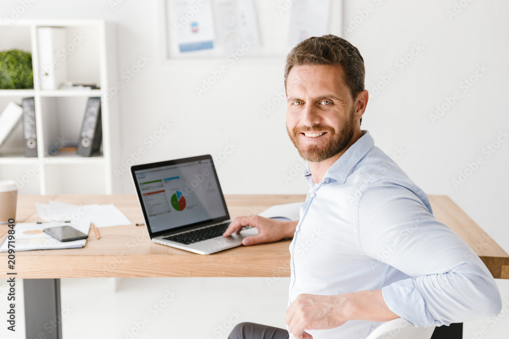Smiling businessman sitting at the desk with laptop computer Smiling businessman sitting at the desk with laptop computer