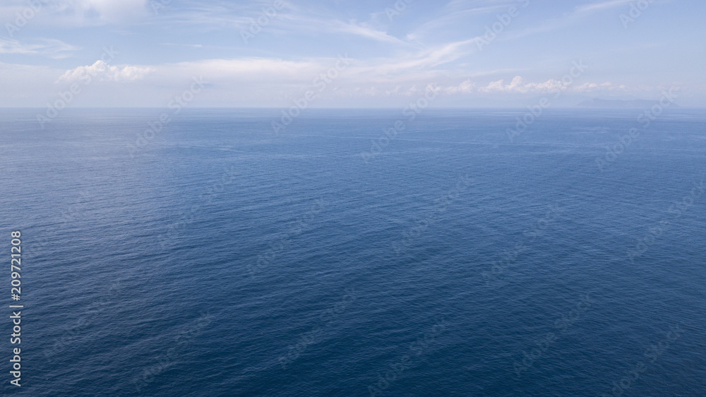 Aerial view of the blue waters of the Mediterranean Sea and specifically of the Tyrrhenian Sea. Sunlight is reflected on the surface of the water. Sky and clouds are on background.