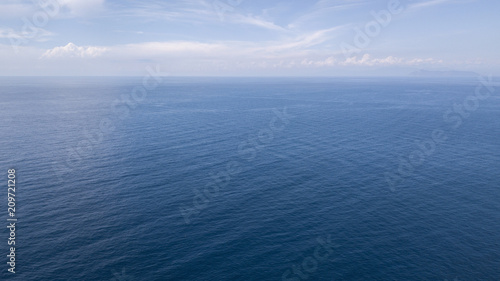  Aerial view of the blue waters of the Mediterranean Sea and specifically of the Tyrrhenian Sea. Sunlight is reflected on the surface of the water. Sky and clouds are on background.