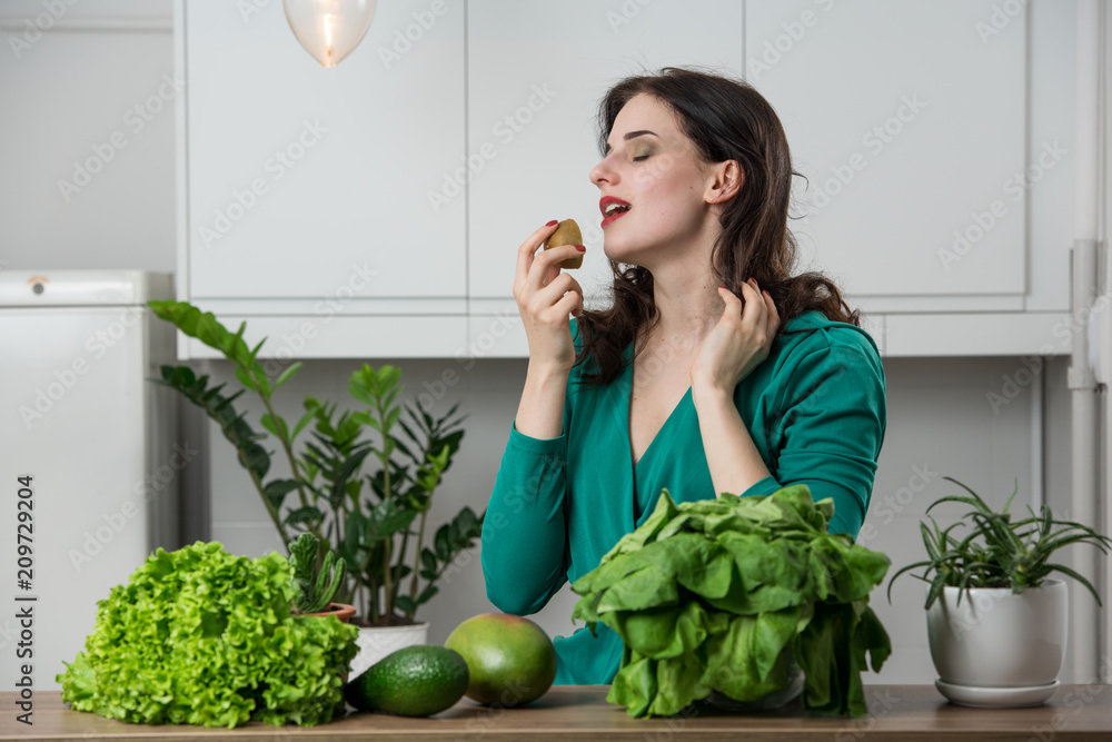 portrait of young woman in a dress eating fruits in the kitchen. Vegetarian concept portrait of young woman in a dress eating fruits in the kitchen. Vegetarian concept