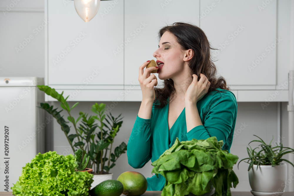 portrait of young woman in a dress eating fruits in the kitchen. Vegetarian concept portrait of young woman in a dress eating fruits in the kitchen. Vegetarian concept