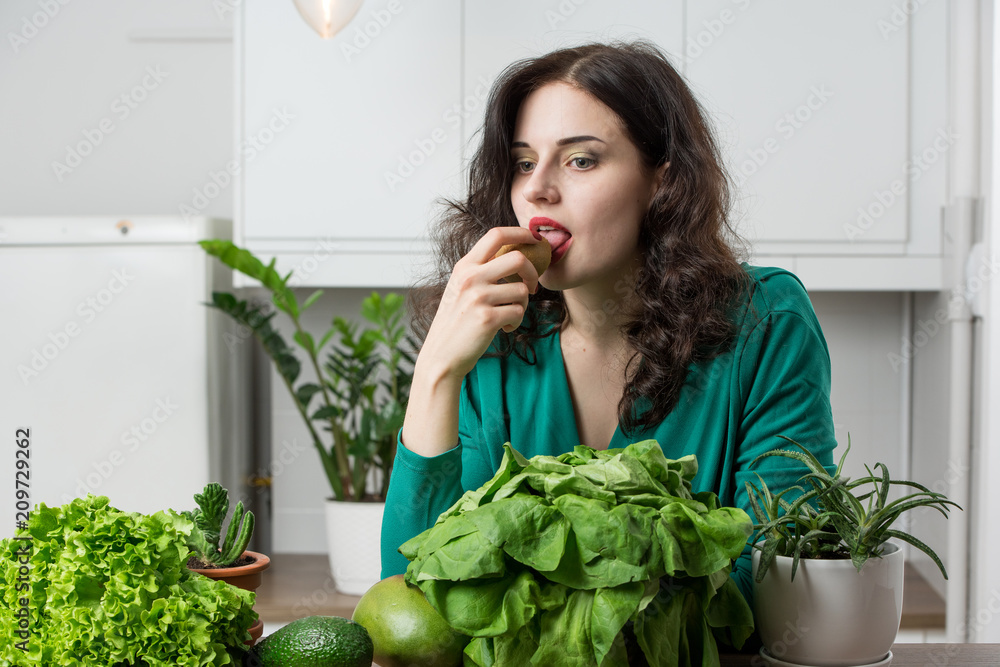 portrait of young woman in a dress eating fruits in the kitchen. Vegetarian concept portrait of young woman in a dress eating fruits in the kitchen. Vegetarian concept