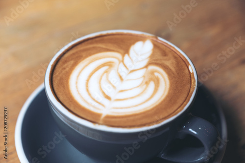 Closeup image of a blue cup of hot latte coffee with latte art on vintage wooden table in cafe