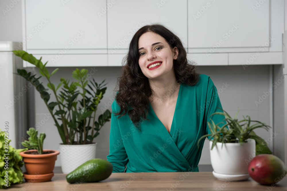 portrait of young woman in a dress surrounded by greenery and fruit in the kitchen. Healthy life