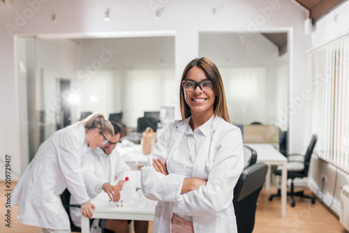Portrait of female scientist or medical worker, colleagues in the background.