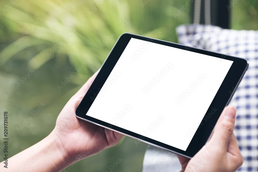 Mockup image of hands holding black tablet pc with white blank desktop screen with green nature background