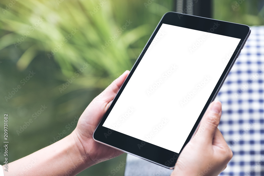 Mockup image of hands holding black tablet pc with white blank desktop screen with green nature background Mockup image of hands holding black tablet pc with white blank desktop screen with green nature background