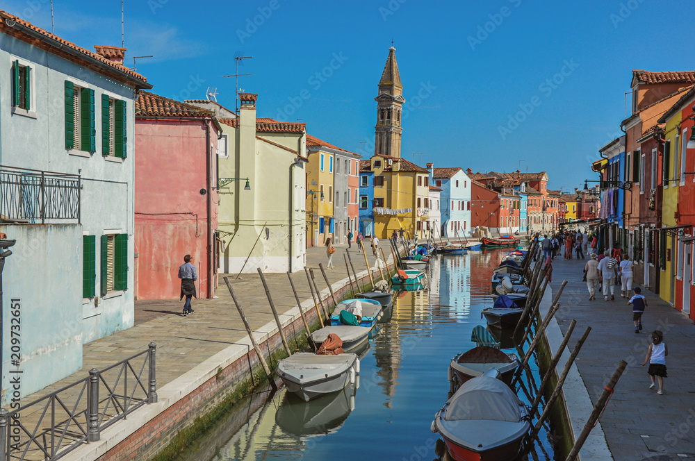 Colorful buildings, tower, people and boats in front of a canal at Burano, a gracious little town full of canals, near Venice. In the Veneto region, northern Italy