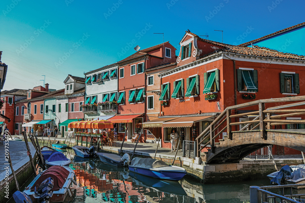 View of colorful buildings, bridge and people in front of a canal at Burano, a gracious little town full of canals, near Venice. In the Veneto region, northern Italy