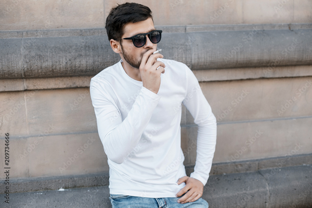 Obraz premium A young man travels through the streets of the city. Boy in sunglasses Stylish man near the building. The man sits on a whip. Beard and hair in a stylish guy.