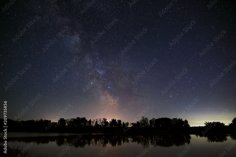 Space with stars in the night sky. The landscape with the river and trees is photographed on a long exposure.