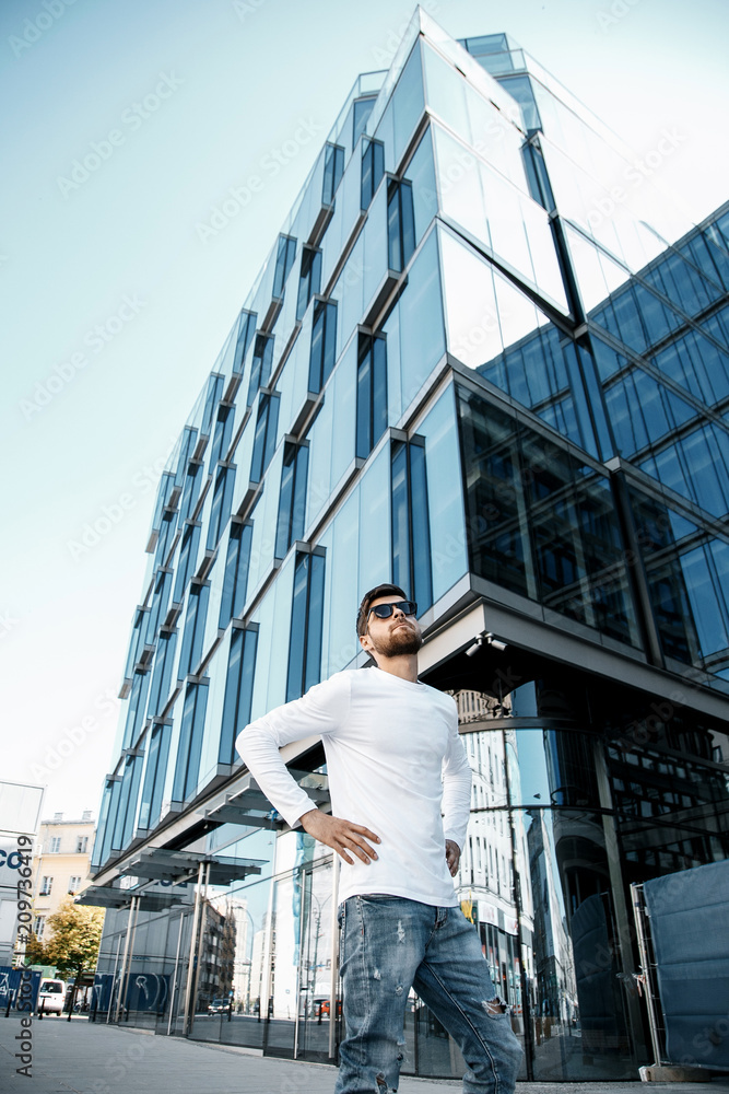A young man travels through the streets of the city. Boy in sunglasses Stylish man near the building. The man sits on a whip. Beard and hair in a stylish guy.