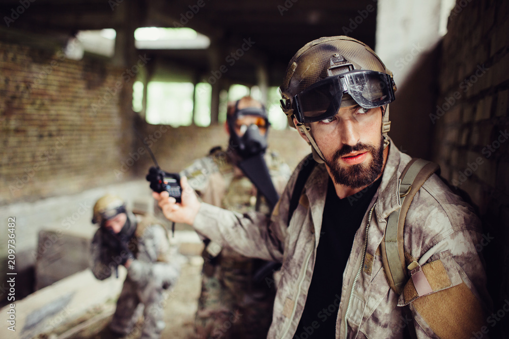 Fototapeta premium Handsome and bearded guy is leaning to wall and looking right. He is careful. Man has stopped his soldiers from attacking. They are waiting.