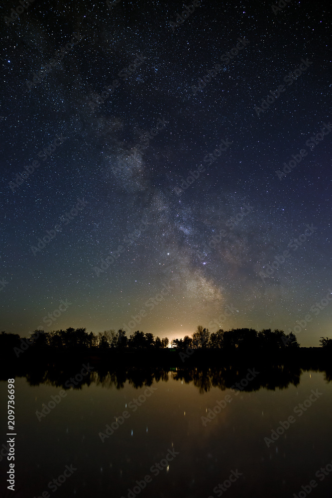 Space with stars in the night sky. The landscape with the river and trees is photographed on a long exposure.