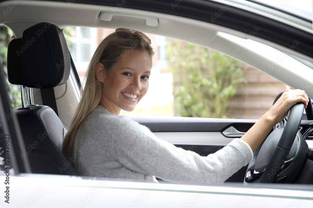 Hübsche blonde Frau am Lenkrad eines Autos schaut lächelnd aus dem Beifahrerfenster Hübsche blonde Frau am Lenkrad eines Autos schaut lächelnd aus dem Beifahrerfenster