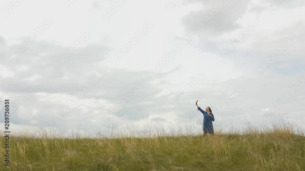 a young woman with red hair and a blue denim dress is in the mountains outside the city and is trying to catch a cellular connection.