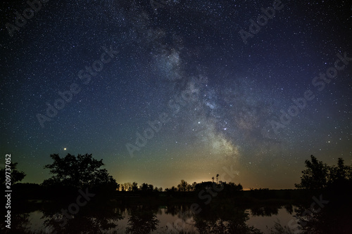 Space with stars in the night sky. The landscape with the river and trees is photographed on a long exposure.