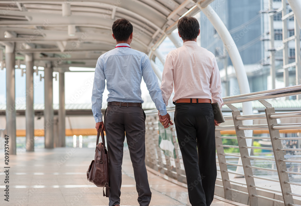 Homosexuality, same-sex marriage, gay and love concept. Close up of happy male gay couple or friends on business clothes hold hands and walking from back Homosexuality, same-sex marriage, gay and love concept. Close up of happy male gay couple or friends on business clothes hold hands and walking from back