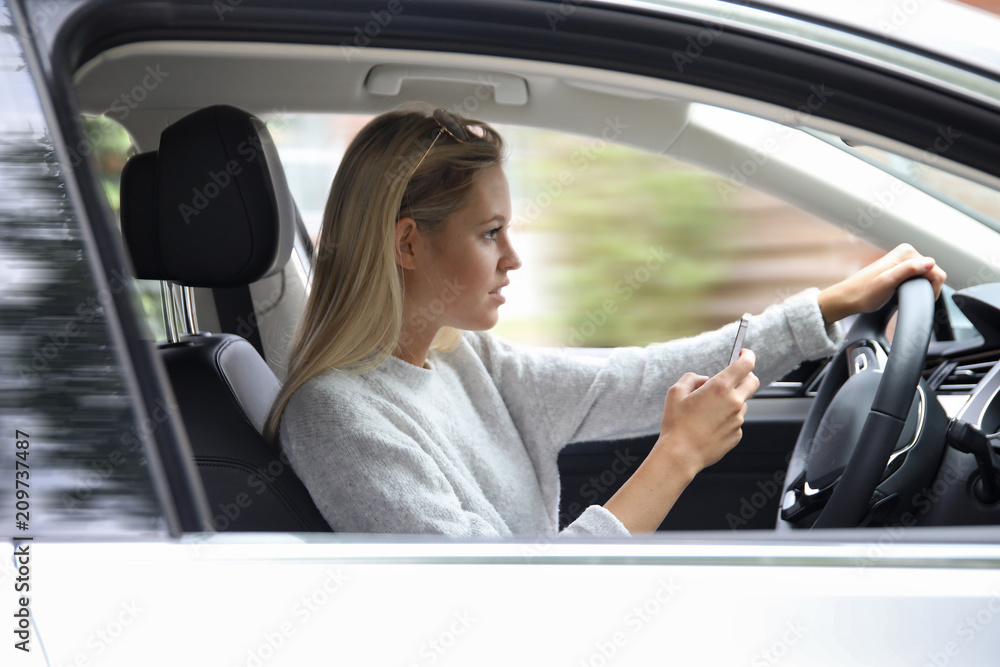 Hübsche blonde Frau hält während des Autofahrens ein Smartphone in den Händen Hübsche blonde Frau hält während des Autofahrens ein Smartphone in den Händen