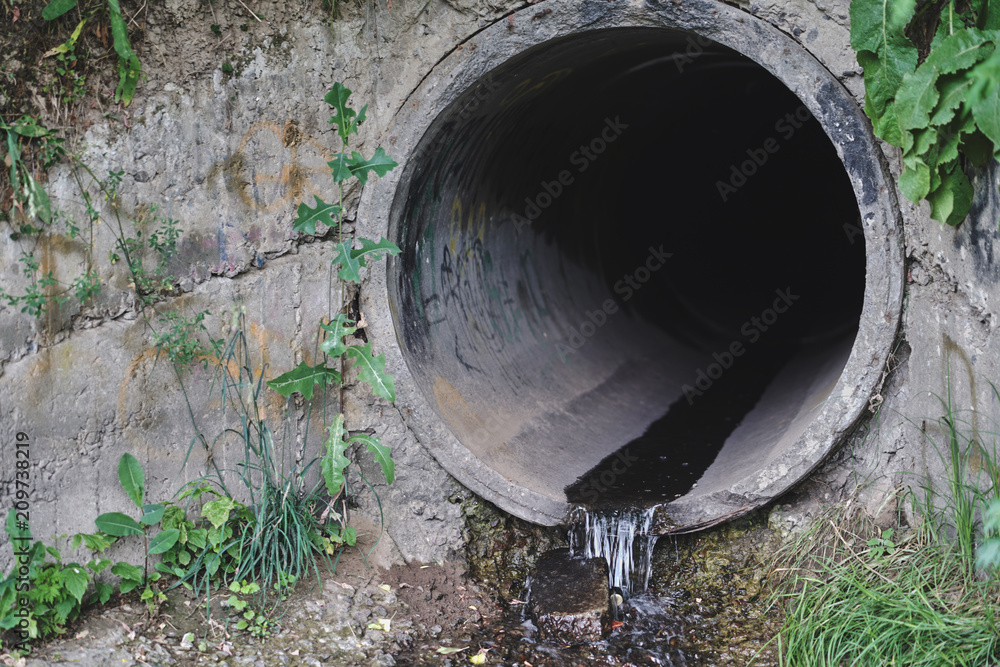 Old concrete and rusty metal, cast-iron drainage pipes in the park. Consolidated wastewater system, leveled in place.