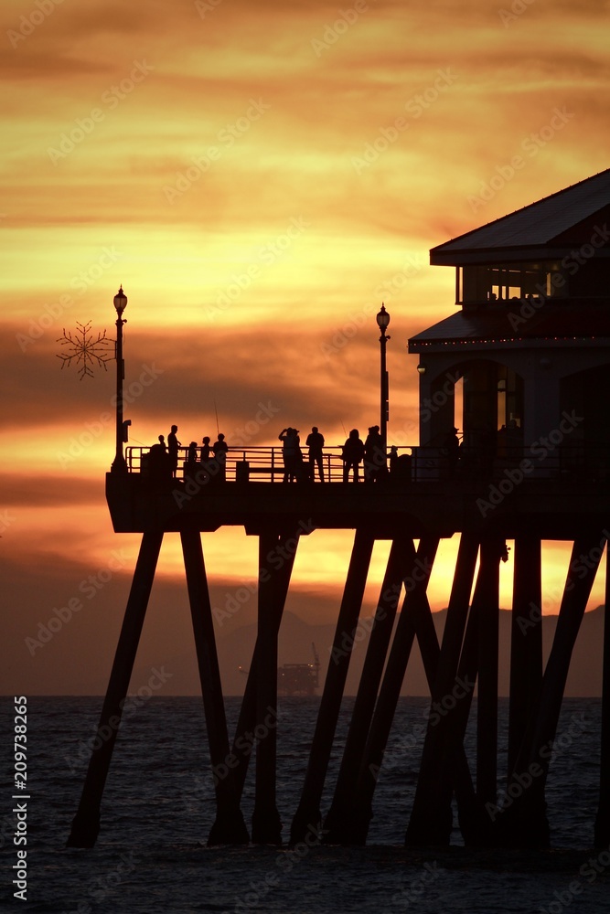 Silhouette of people standing on the end of the Huntington Beach pier during an orange sunset sky