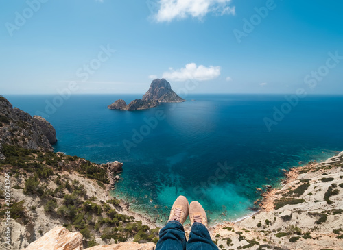 piernas y pies de mujer colgado de acantilado del parque natural de cala D´hort. Al fondo se observan los islotes de Es Vedrá y Es Vedranell, Ibiza, España photo