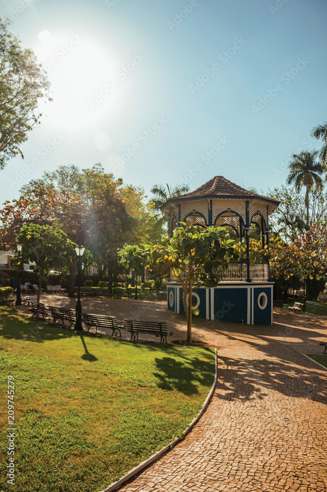Old and colorful gazebo of square in the middle of verdant garden full of trees, in a bright sunny day at São Manuel. A cute little town in the countryside of São Paulo State. Southeast Brazil.	