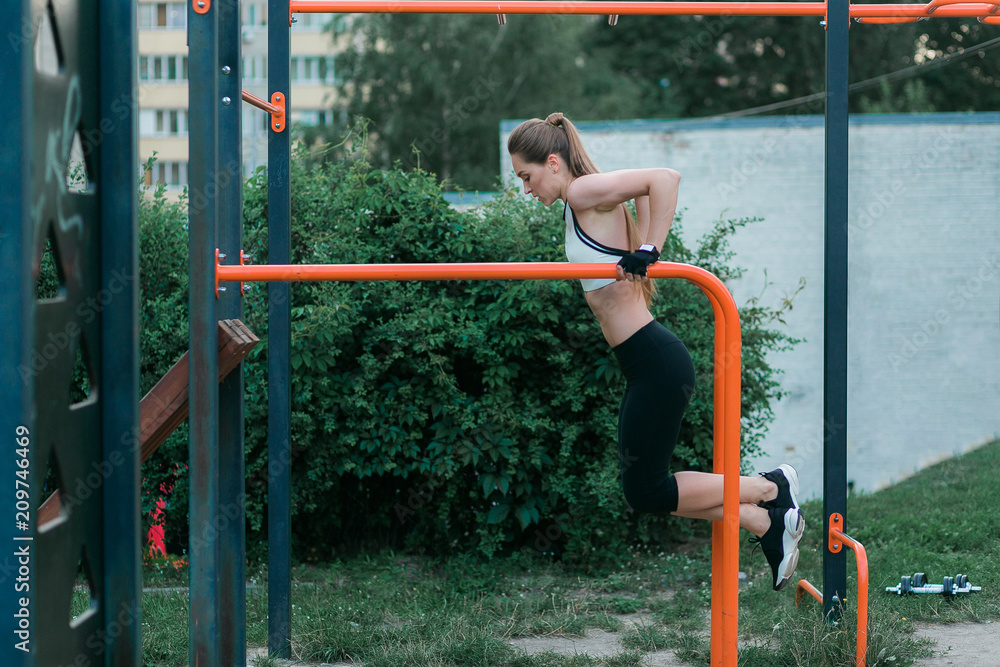 Strong and physically fit young woman doing triceps dips on parallel bars at park. Caucasian fitness female exercising outdoors