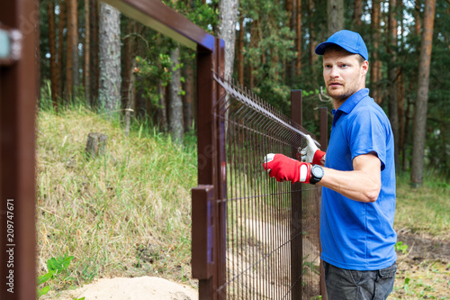 man installing brown metal fence