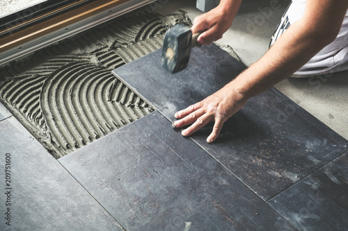 Tableau sur toile Worker placing anthracite ceramic floor tiles on adhesive surface
