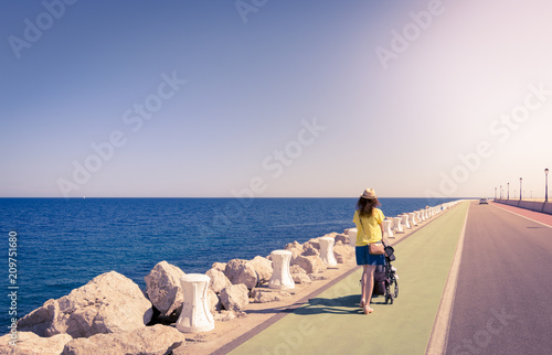 Mother strolling with newborn in a coast long road